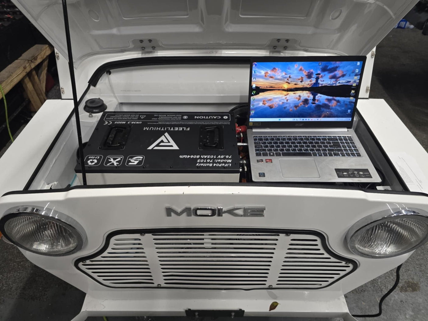 Fleet Lithium MOKE America EV (2018-Present) (72V) Fleet Lithium Conversion Kit installed in the front compartment of a white MOKE America EV, with a laptop open next to the battery showing monitoring software.