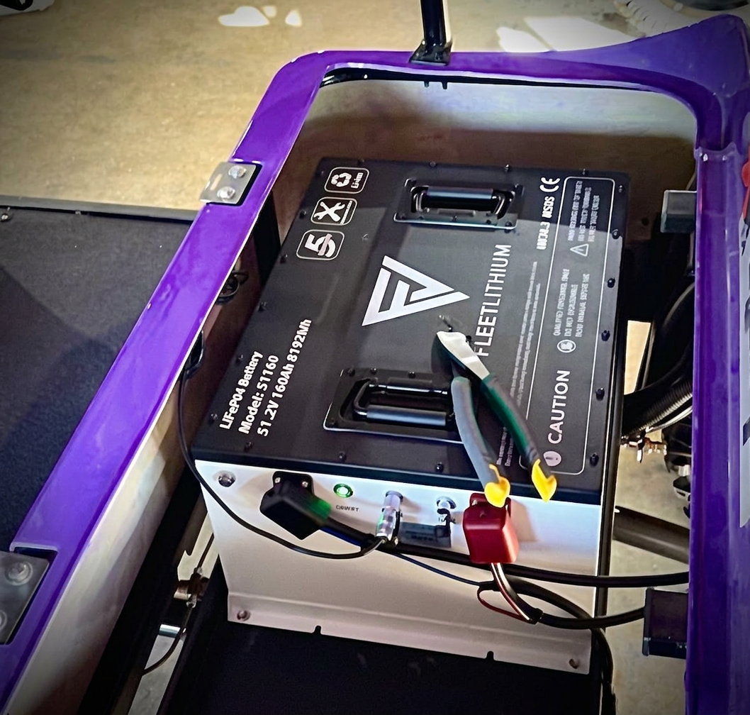 FleetLithium battery with cables and pliers installed in a purple vehicle.