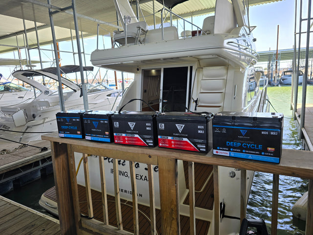 Fleet Lithium BlueMax Marine 12V 195Ah LiFePO4 Deep Cycle Battery (Group 27) lined up on a wooden railing with a boat in the background.
