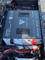 A FleetLithium lithium-ion battery pack installed inside a black metal frame or vehicle compartment, with wiring, connectors, and tools visible around it in an outdoor setting.